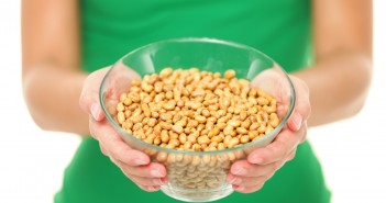 Dried salty soybeans - healthy snack. Woman showing asian snack: dry soya beans isolated on white background in studio.