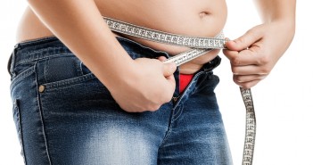 Overweight woman wearing jeans measuring her fat body belly paunch